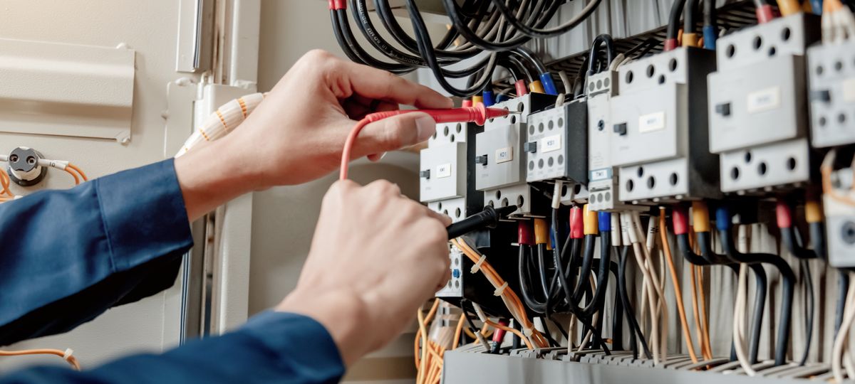 Technician probing terminals inside an ageing DC power cabinet